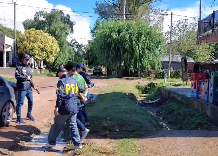 El detenido está esposado y ahora es escoltado por dos agentes de la Policía Federal, mientras uno porta un arma larga y los espera en un movil.